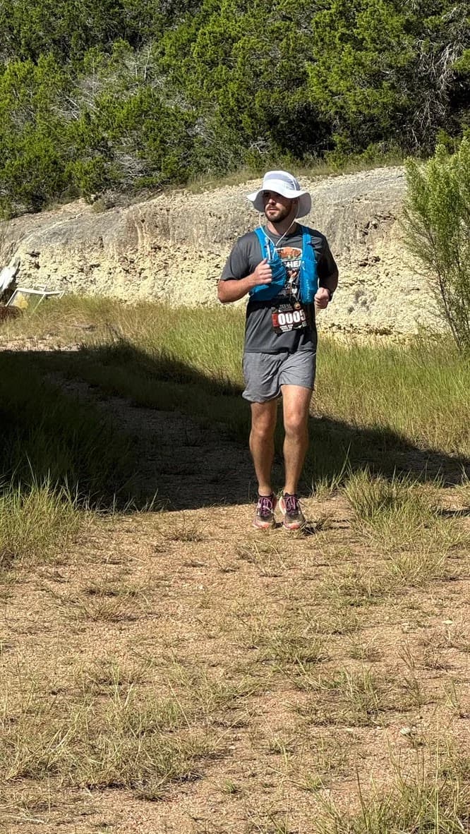 Dylan running a dry trail section in a sun hat and hydration vest.