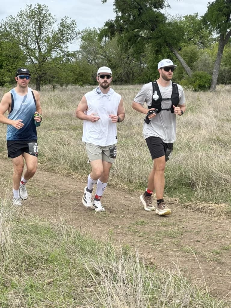 Dylan running a muddy trail loop alongside two other runners.
