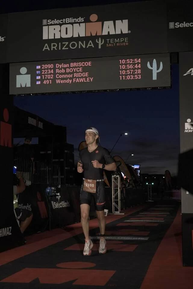 Dylan running down the Ironman Arizona finish chute at night, his name at the top of the finish board.